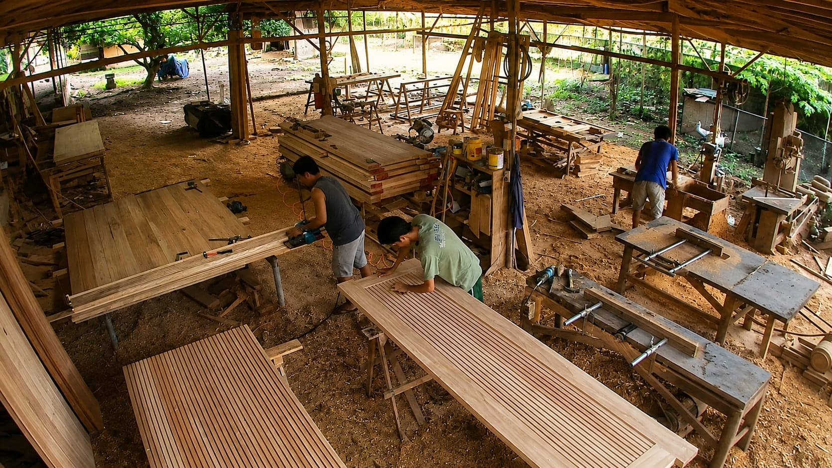OLAZO's open-sided workshop, with craftsmen working across fluted door panels laid out on trestles